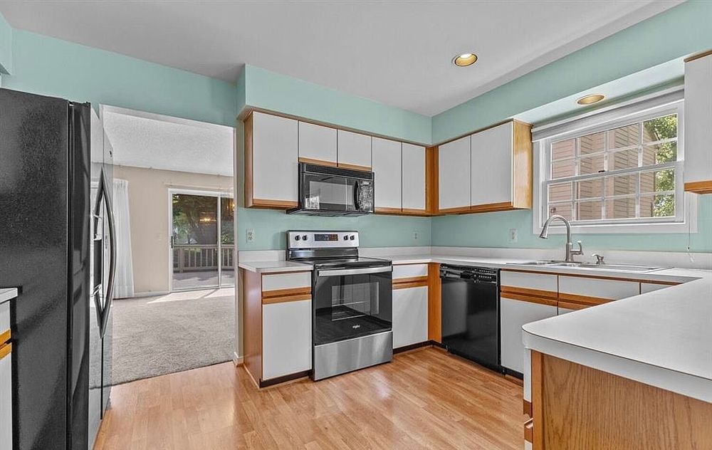 Bright kitchen with stainless steel appliances, white cabinetry, wood trim accents, hardwood floors, and mint green painted walls.
