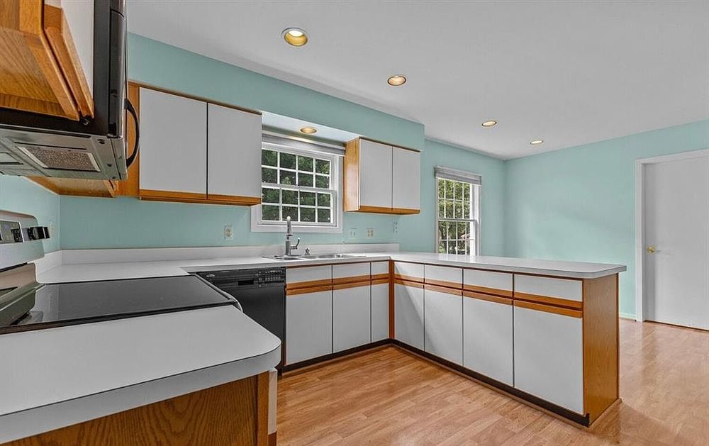 Kitchen featuring white cabinets with wood trim, peninsula island, light hardwood floors, and mint green walls with ample counter space.