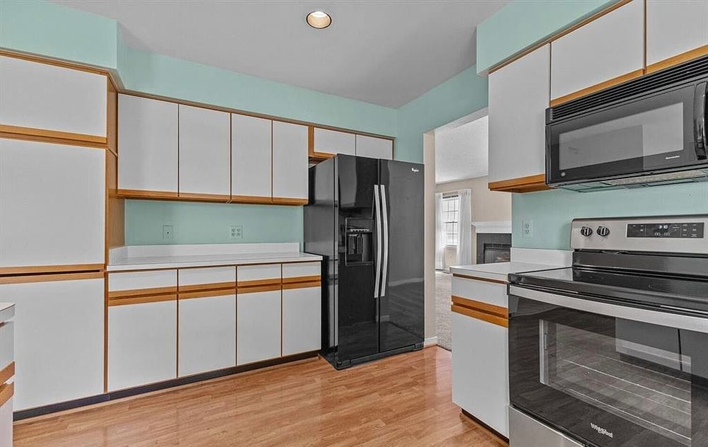 Kitchen with white upper cabinets, black refrigerator, white range, built-in microwave, and light hardwood flooring throughout.