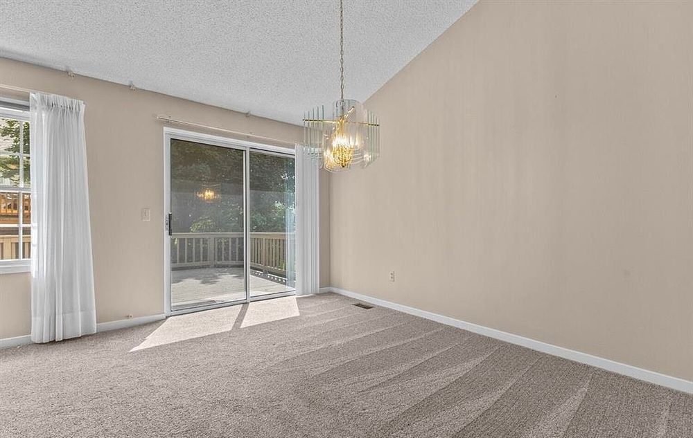 Carpeted dining area with vaulted ceiling, chandelier, and sliding glass door opening to outdoor deck.