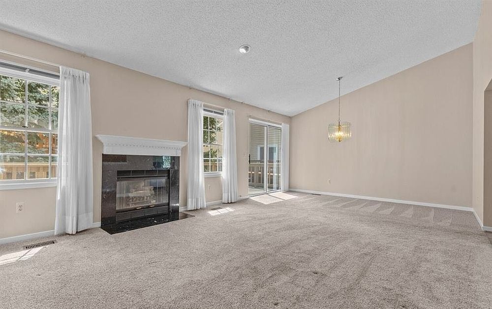 Spacious living room with neutral carpet, fireplace, large windows, and sliding glass doors flooding the space with natural light.