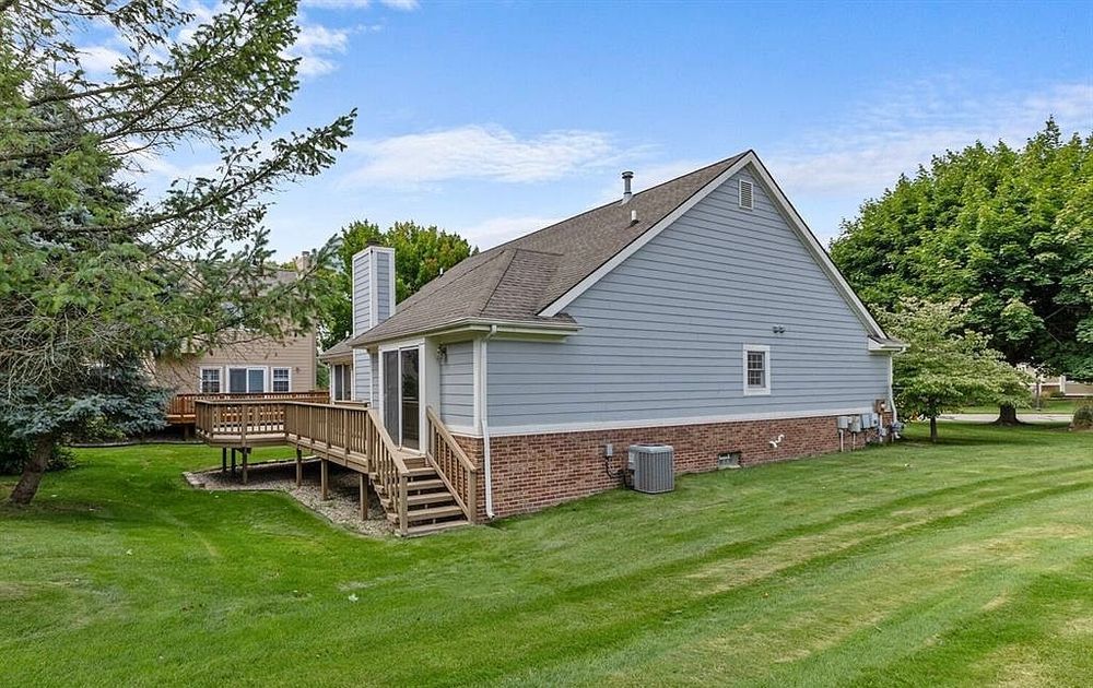 Rear exterior of a gray vinyl-sided home with brick foundation, wooden deck, and lush green lawn.