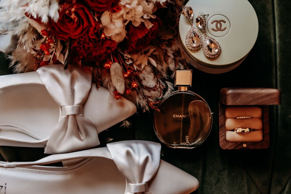 A collection of vintage-style wedding details featuring red roses, gold jewelry, and silk ribbons in warm moody lighting.