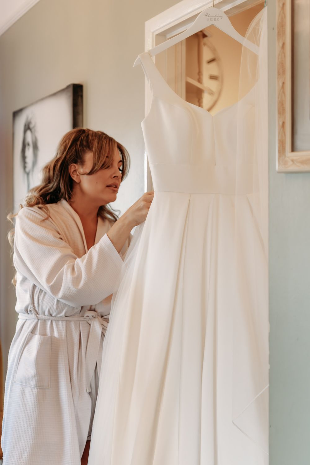 Person in white robe smelling clean laundry hanging on clothesline in bright interior setting.