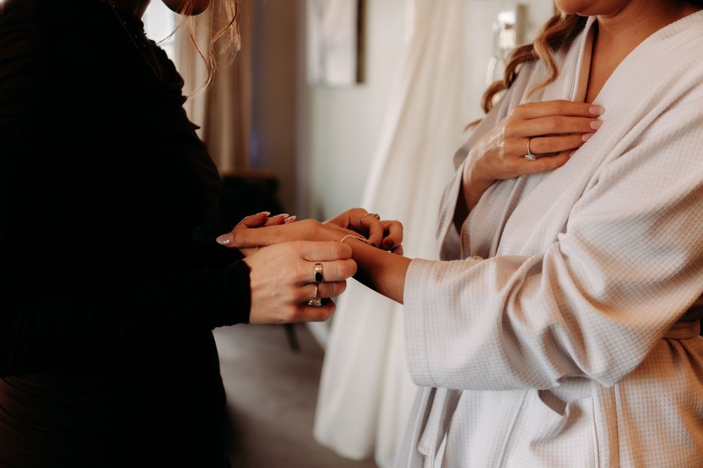 Person in white shirt adjusts sleeves in soft natural lighting against neutral background.
