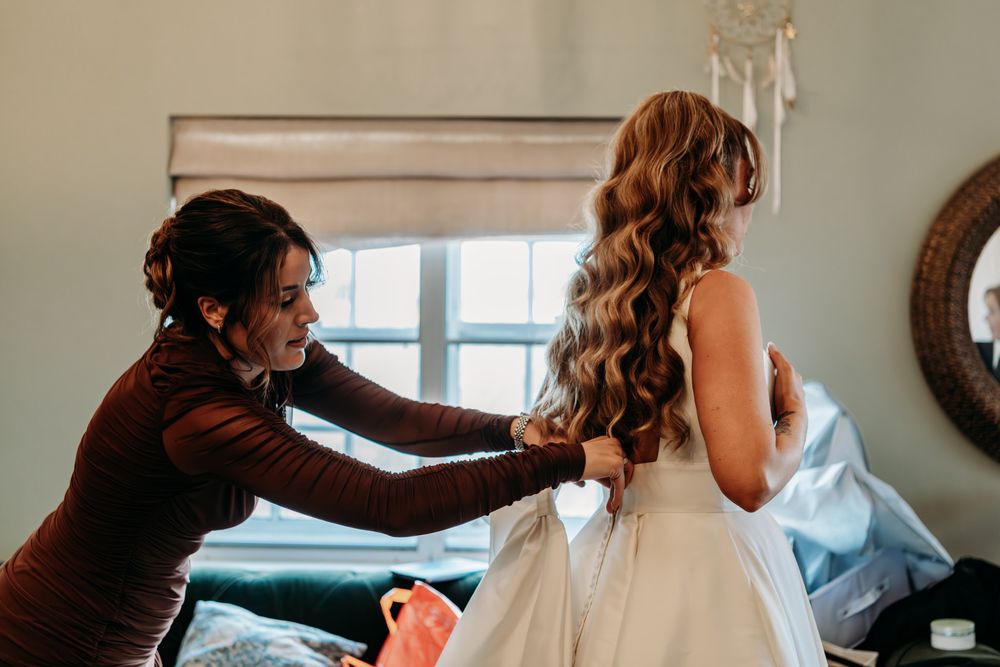 A wedding day preparation scene showing final touches being made to a bride's hair and dress.