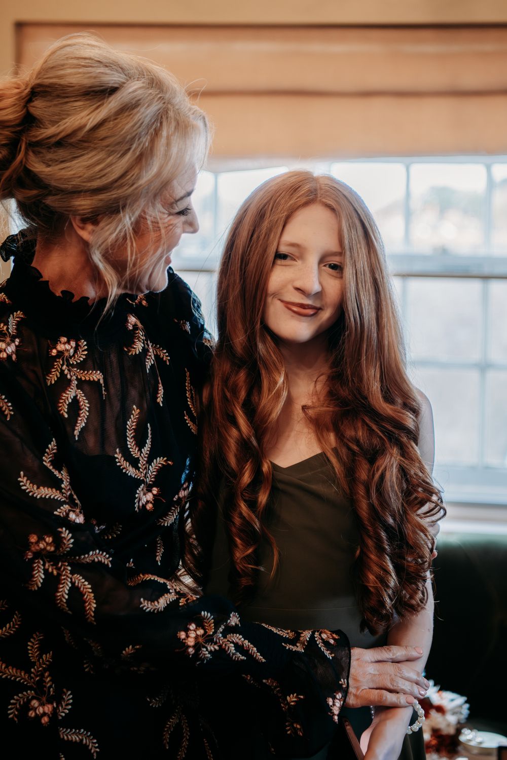 Two people share a joyful moment while wearing dark clothing in a sunlit room.