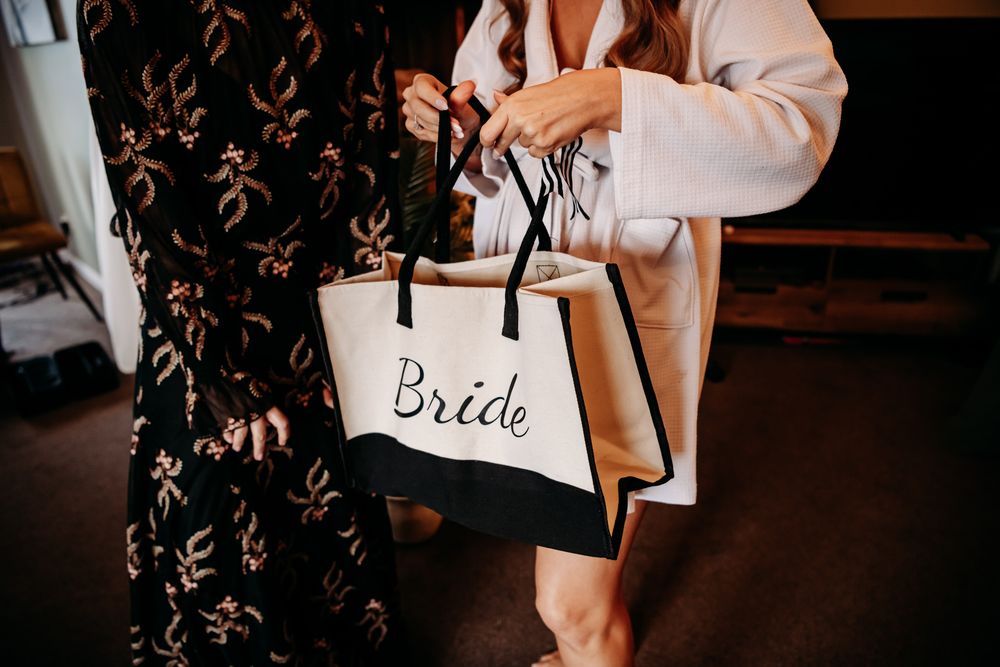A white canvas tote bag with 'Bride' text being held at a wedding event.