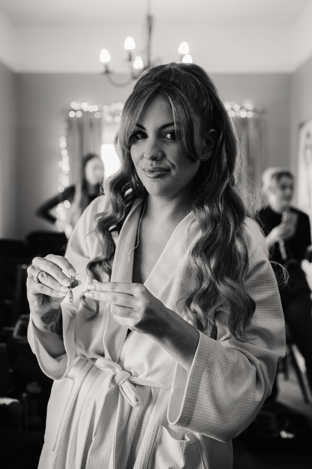 Black and white photo of someone in a white robe getting ready with hair styled in loose waves, standing in a room.
