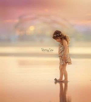 Young girl in sequin romper stands reflectively on shallow water at golden sunset.