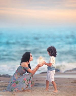 Mother and child share a magical glowing lantern moment on a beach at sunset.