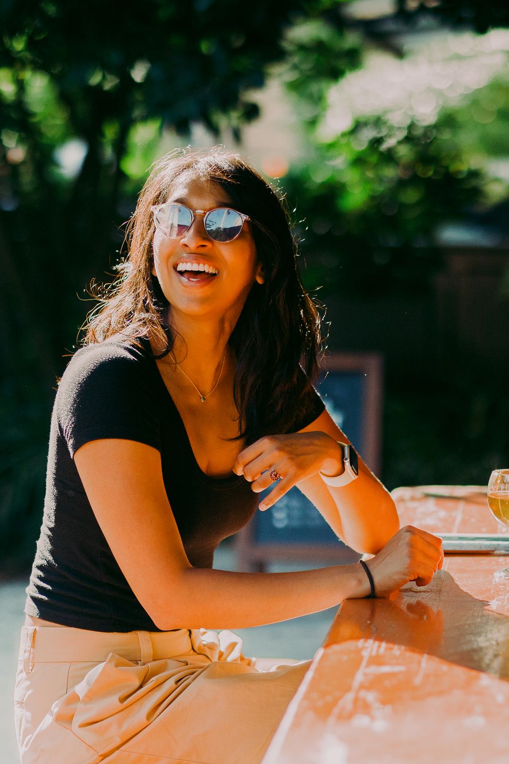 Person in sunglasses laughing while relaxing at an outdoor table.