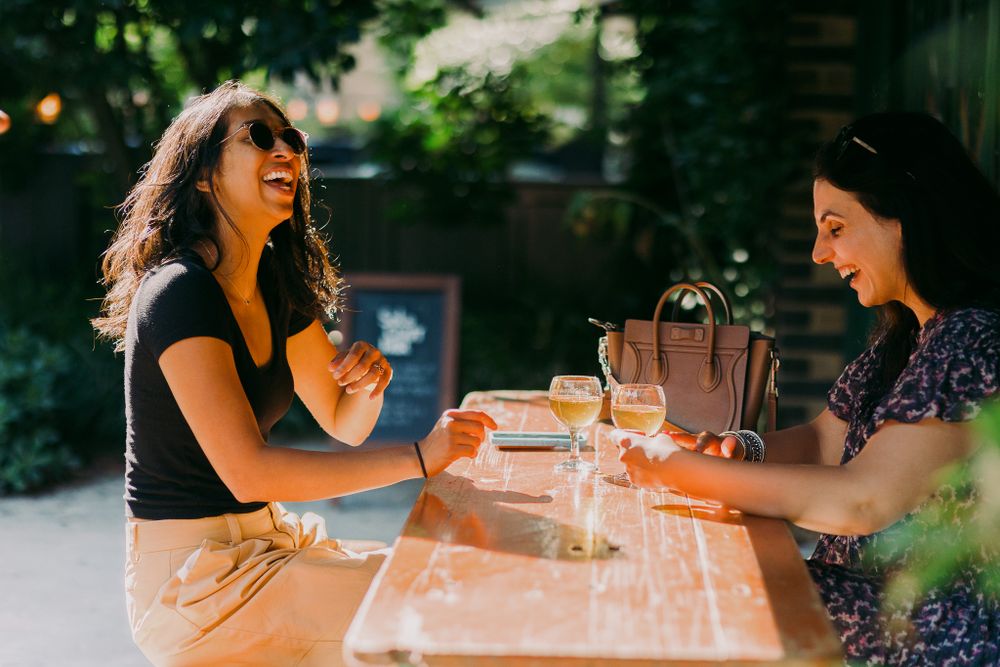 Friends enjoying drinks and conversation at a sunny outdoor table.