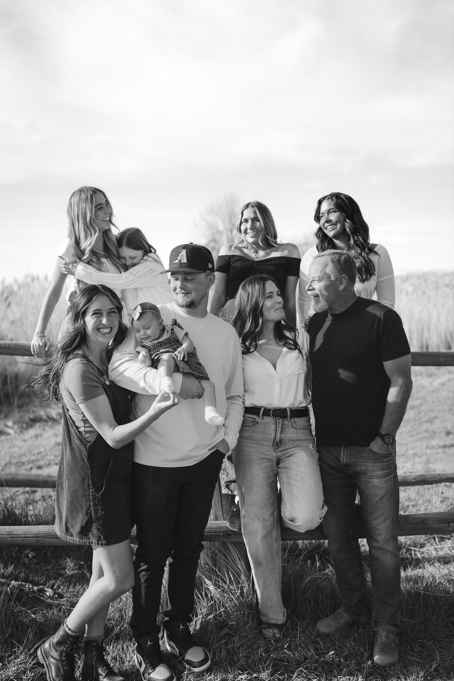 Black and white family portrait of eight people gathered at a wooden fence in a rural outdoor setting.