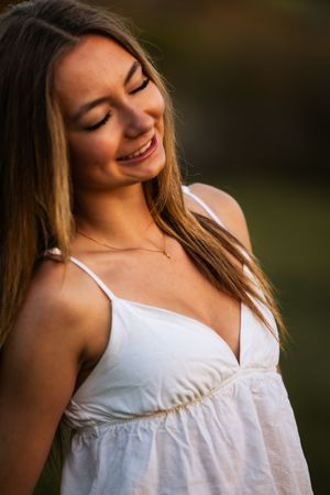 Smiling young woman with long hair wearing a white sundress outdoors in warm golden sunlight.