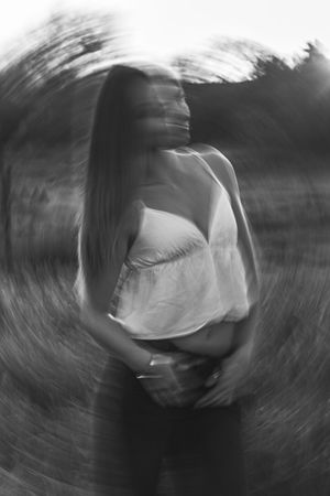 Black and white radial blur portrait of a woman in a white top standing in a field with trees in the background.