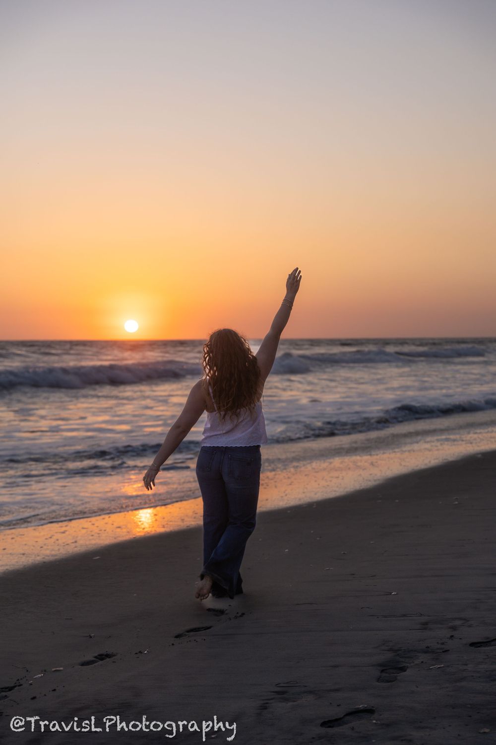 Silhouette of person dancing and jumping on beach at sunset.