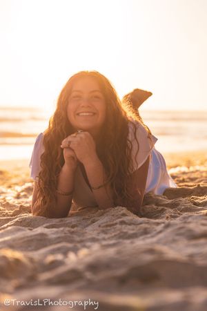 Person lying on beach sand during golden hour sunset with ocean waves in background.