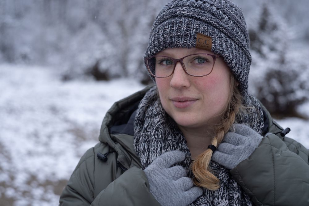 blonde woman wearing winter jacket and stocking hat in snowy scene