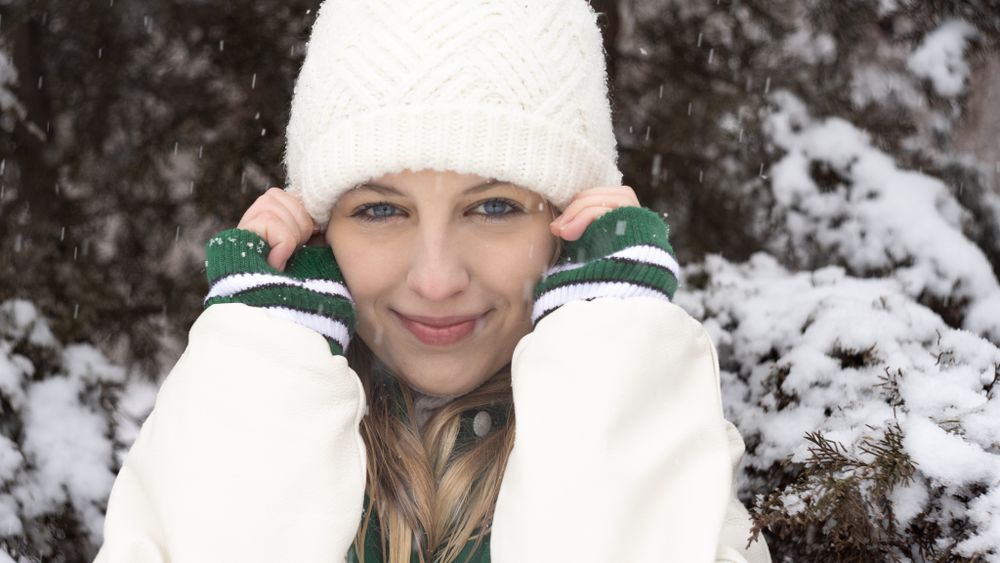closeup portrait of blonde girl in white stocking cap with hands on hat