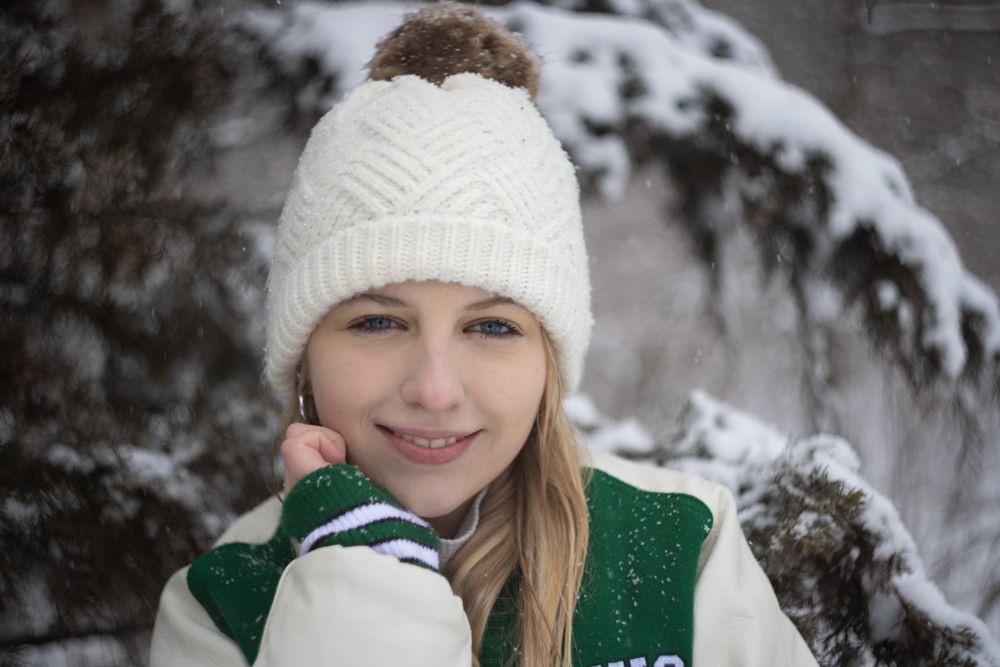 blonde girl in white stocking cap and green letterman jacket in snow