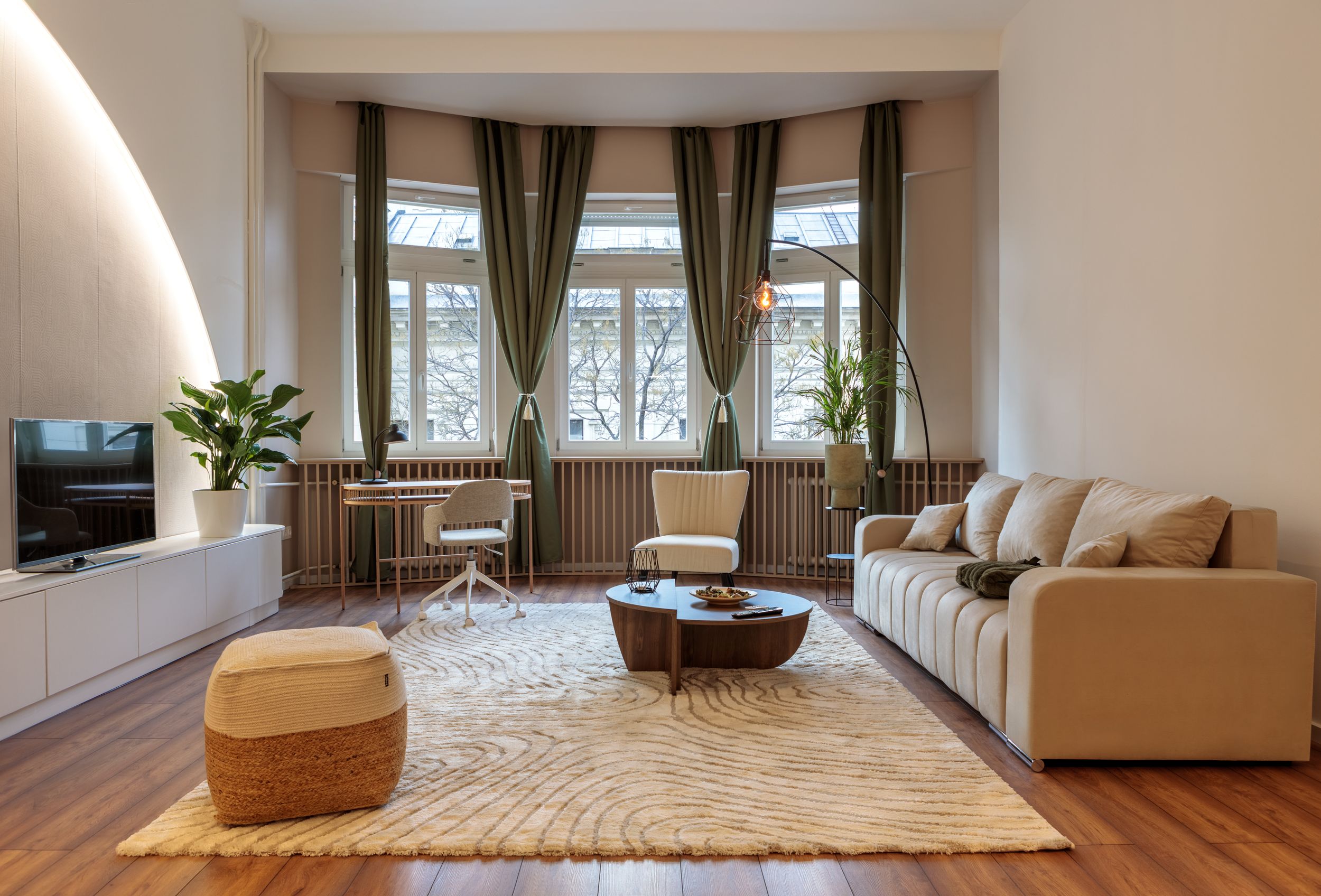 Elegant living room with bay window, green curtains, and beige sofa on patterned area rug.