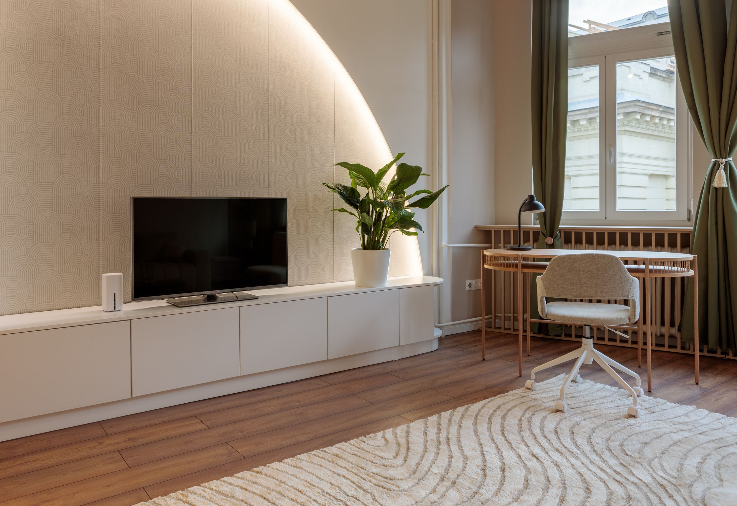 Modern living room with mounted TV, white storage unit, and indoor plant against curved wall.