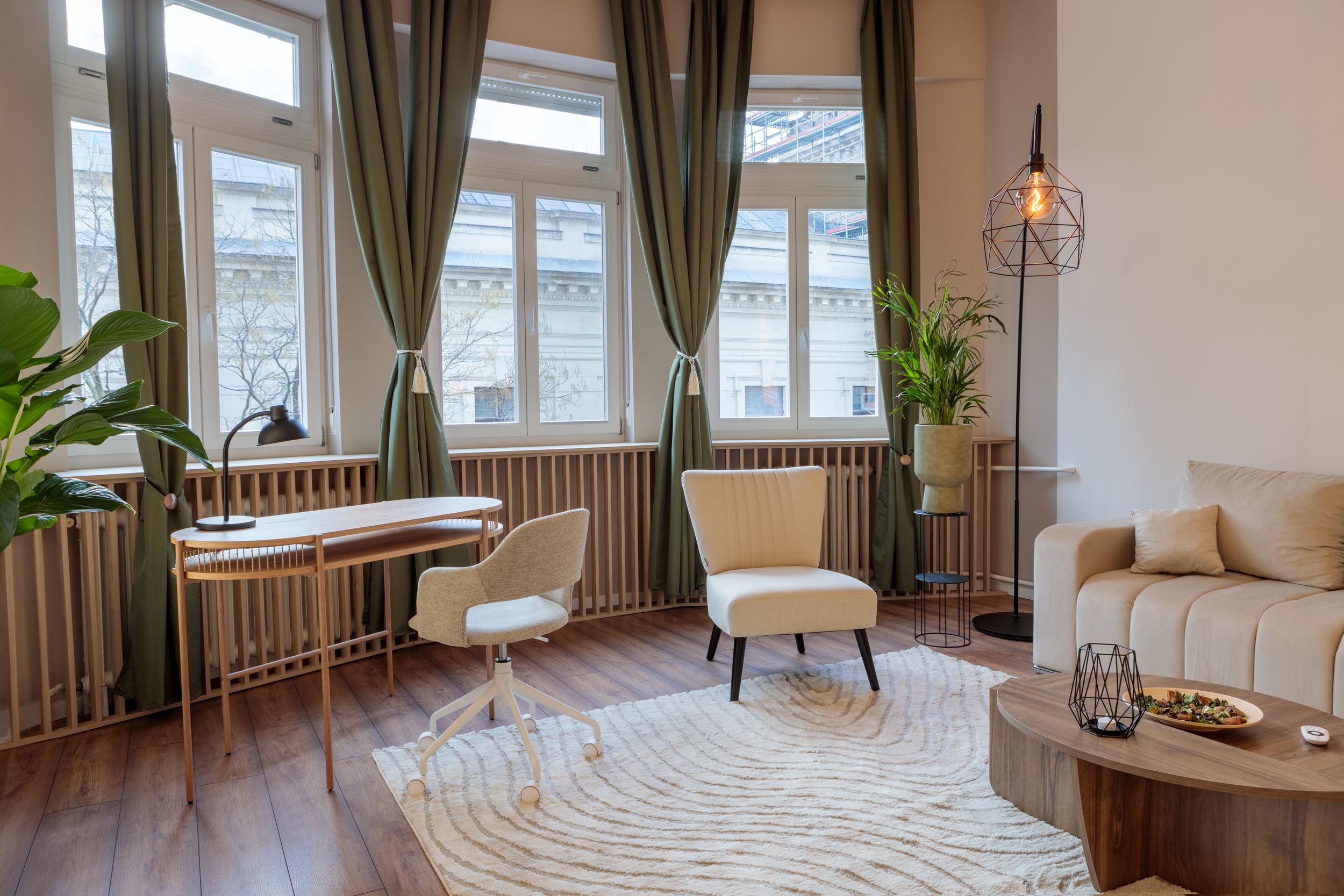 Modern living room with green curtains, round rug, curved sofa and indoor plants by large windows.
