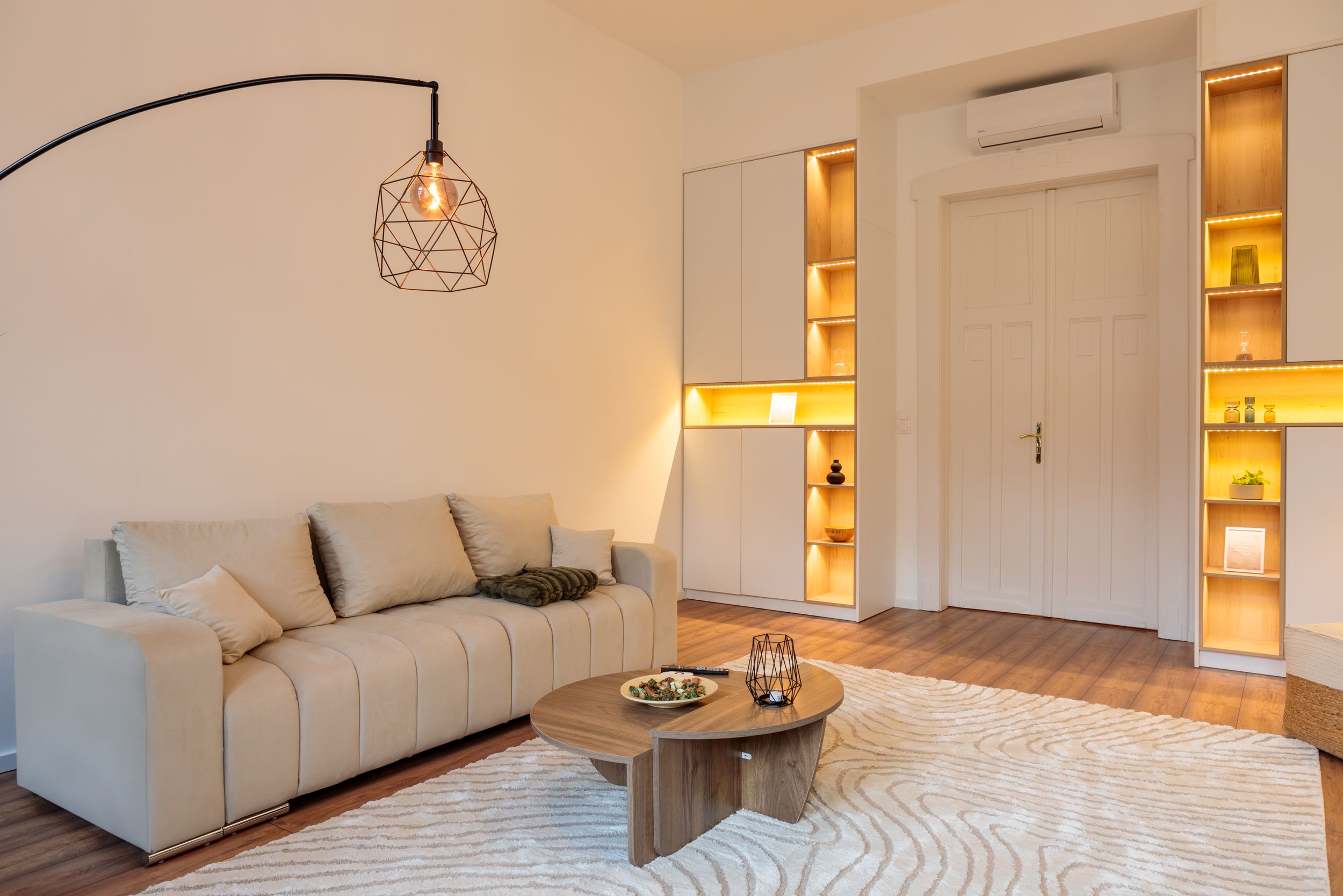 Modern living room featuring arched floor lamp, white sofa, and illuminated built-in shelving.