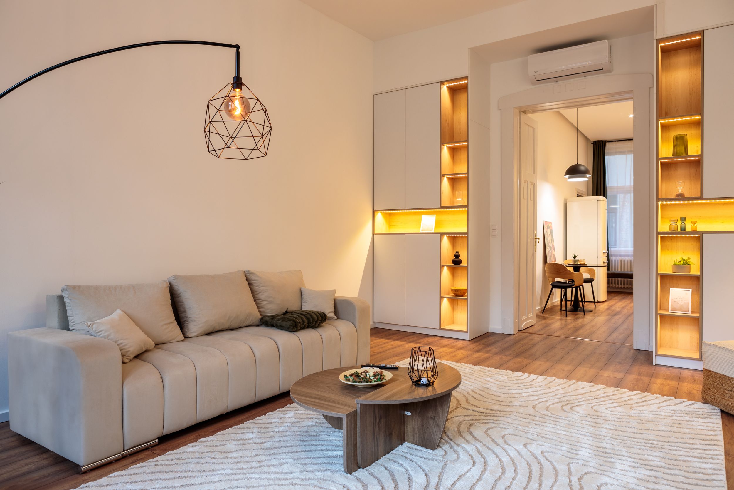 Contemporary living area with grey sofa, arched floor lamp, and illuminated built-in shelving.