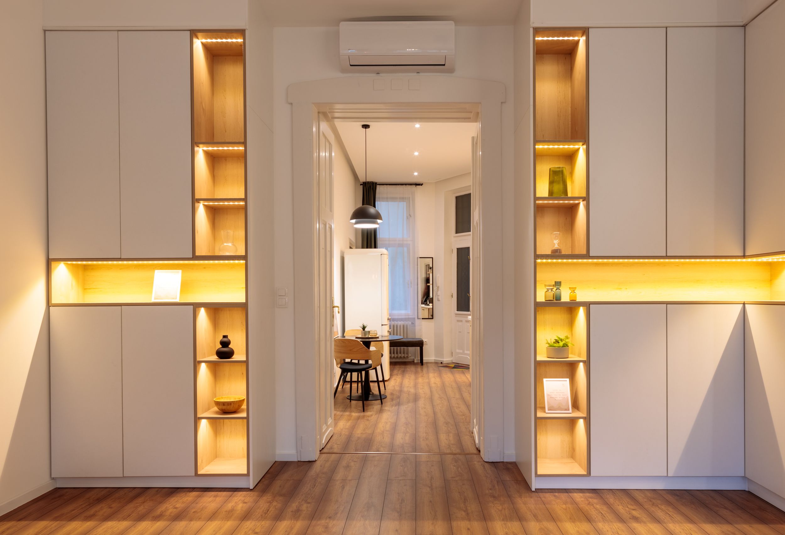 Hallway with illuminated built-in storage cabinets and wooden flooring.