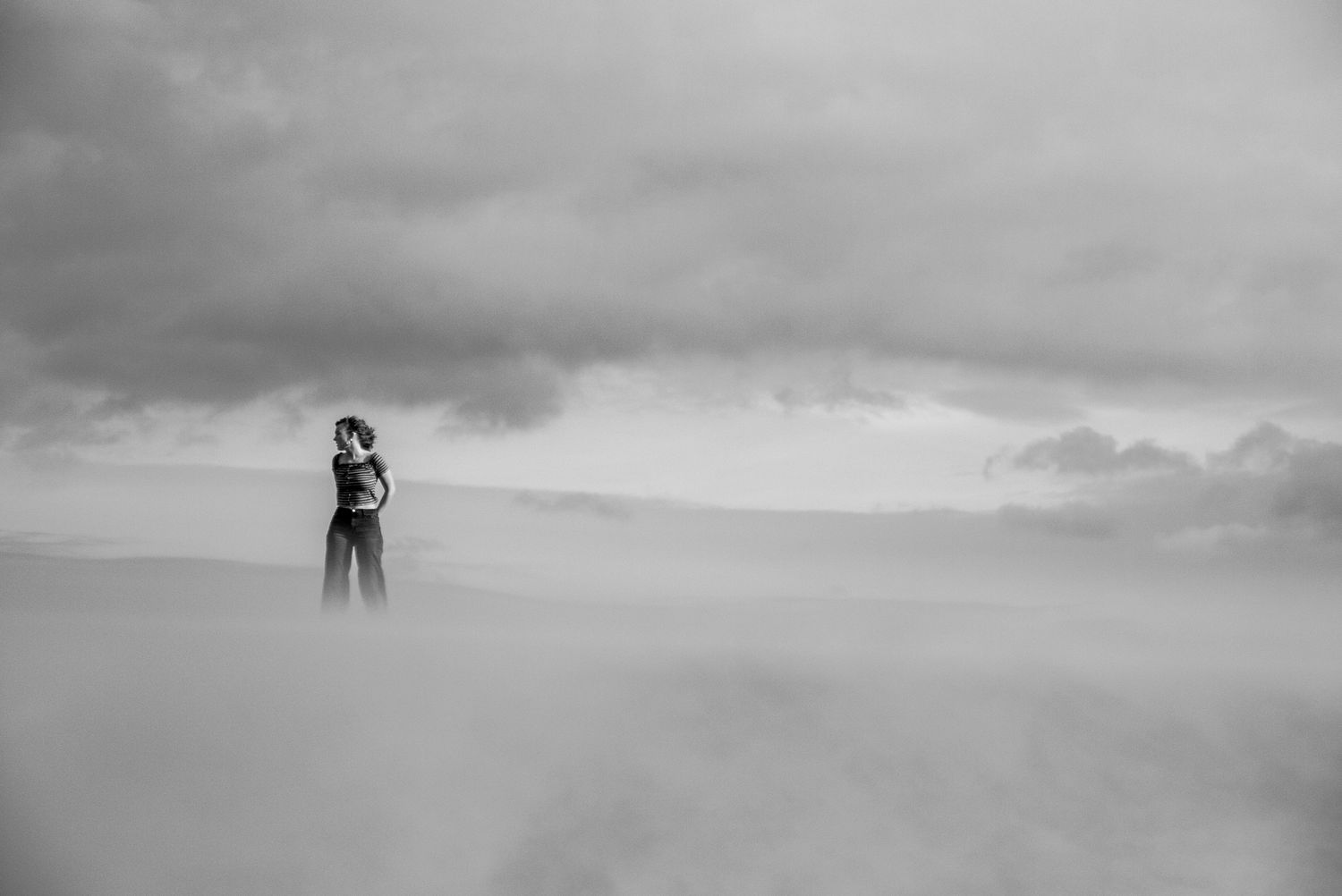black and white photograph of a young woman standing in a hazy field of clouds