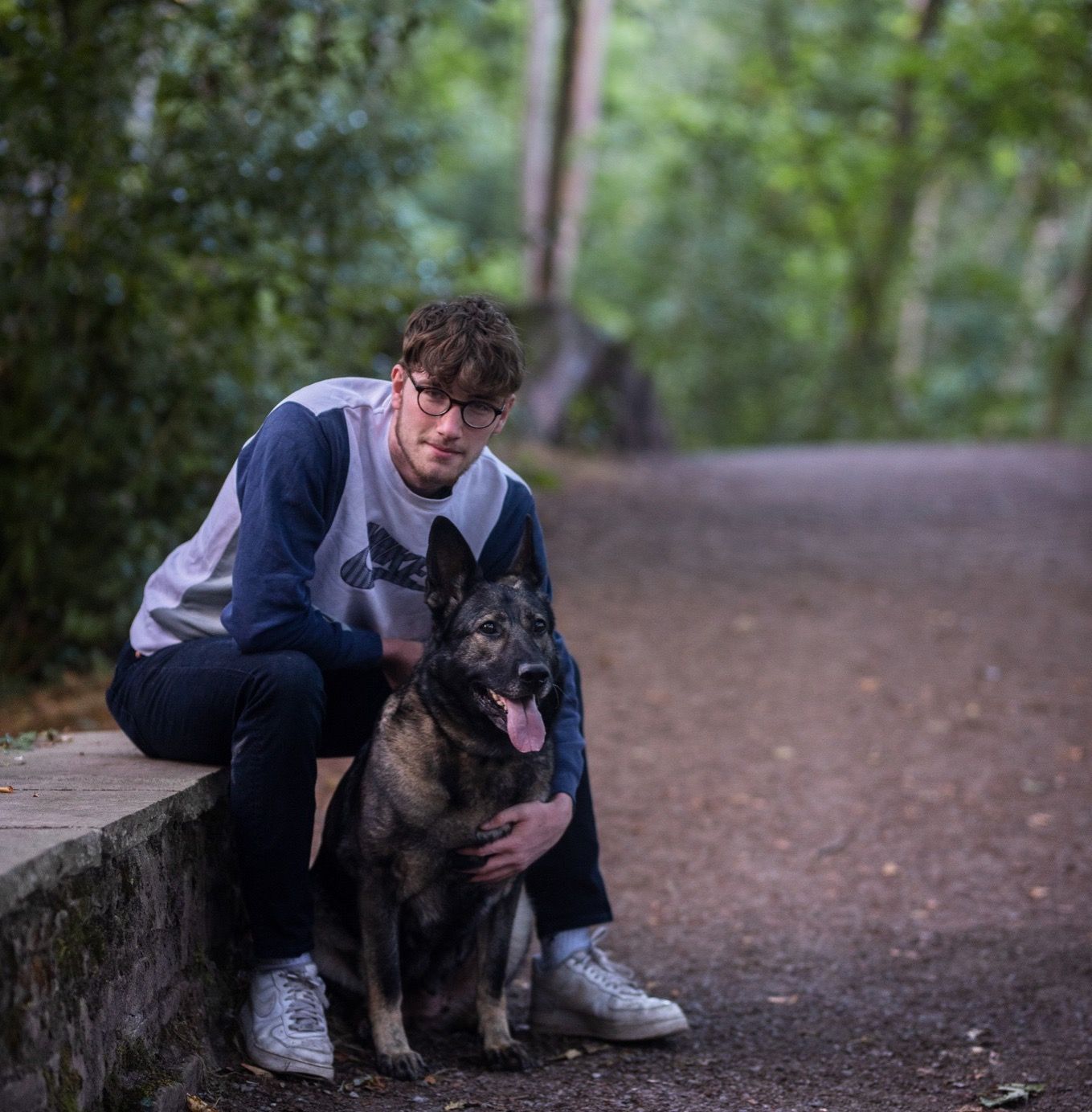 German Shepherd dog and companion enjoying a walk in wooded park setting.