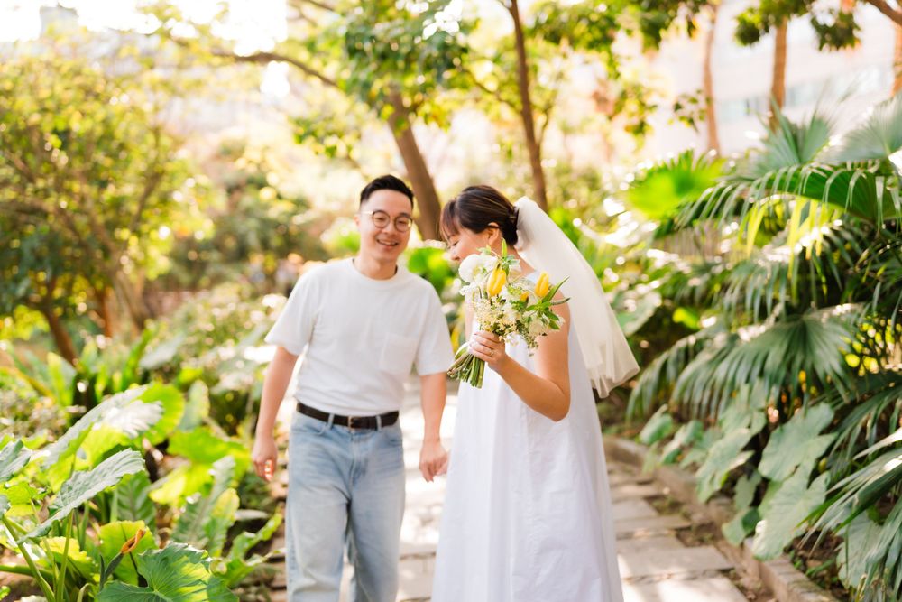 A couple walking through a lush tropical garden path in afternoon sunlight.