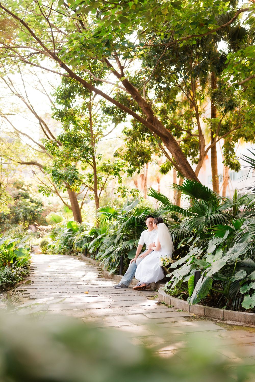 A peaceful garden scene with someone seated on a path surrounded by tropical plants.
