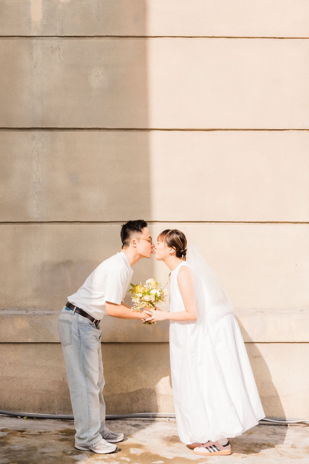 A tender moment shared between a couple holding flowers against a beige wall.