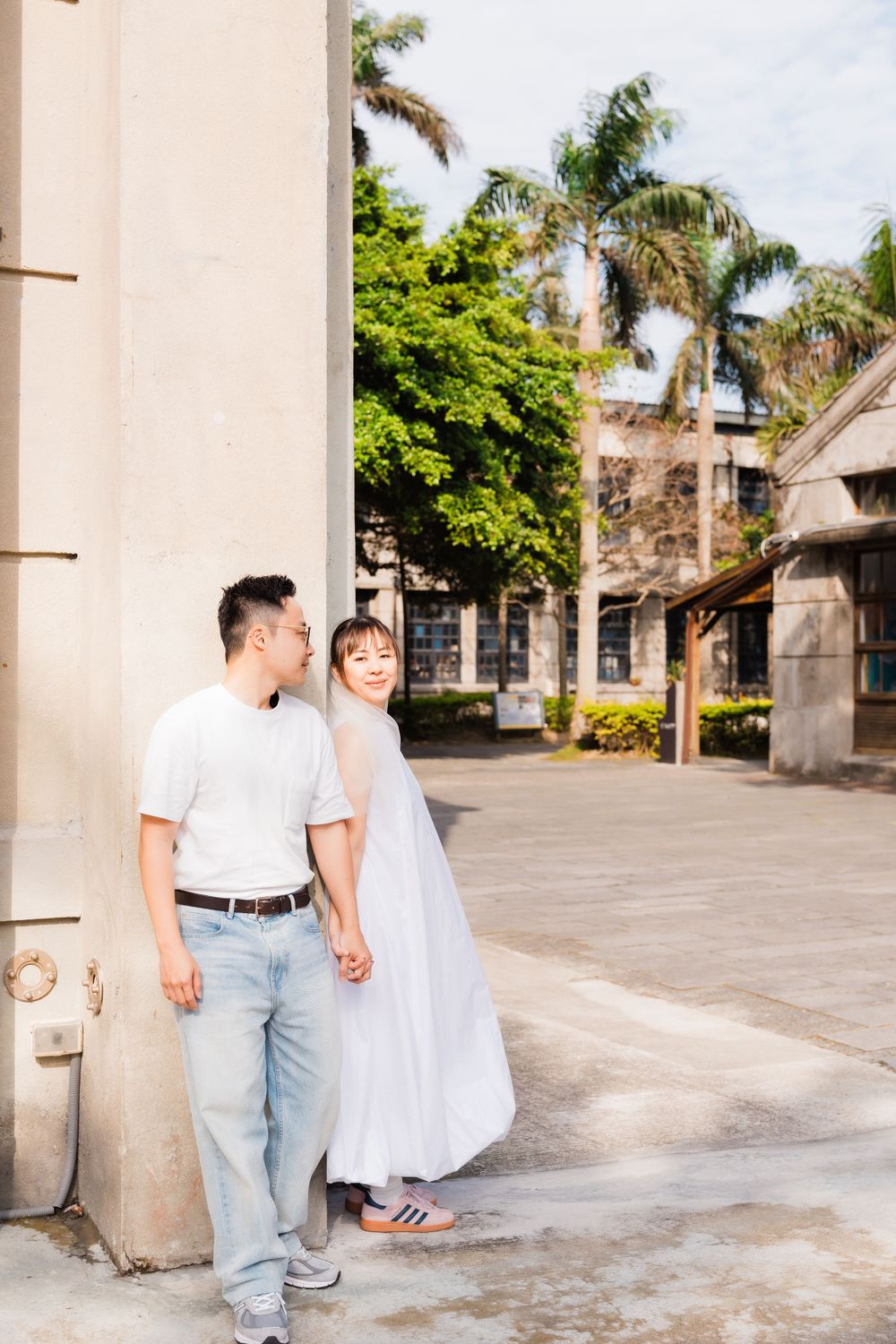 A couple in casual white outfits stroll together on a palm-lined pathway.