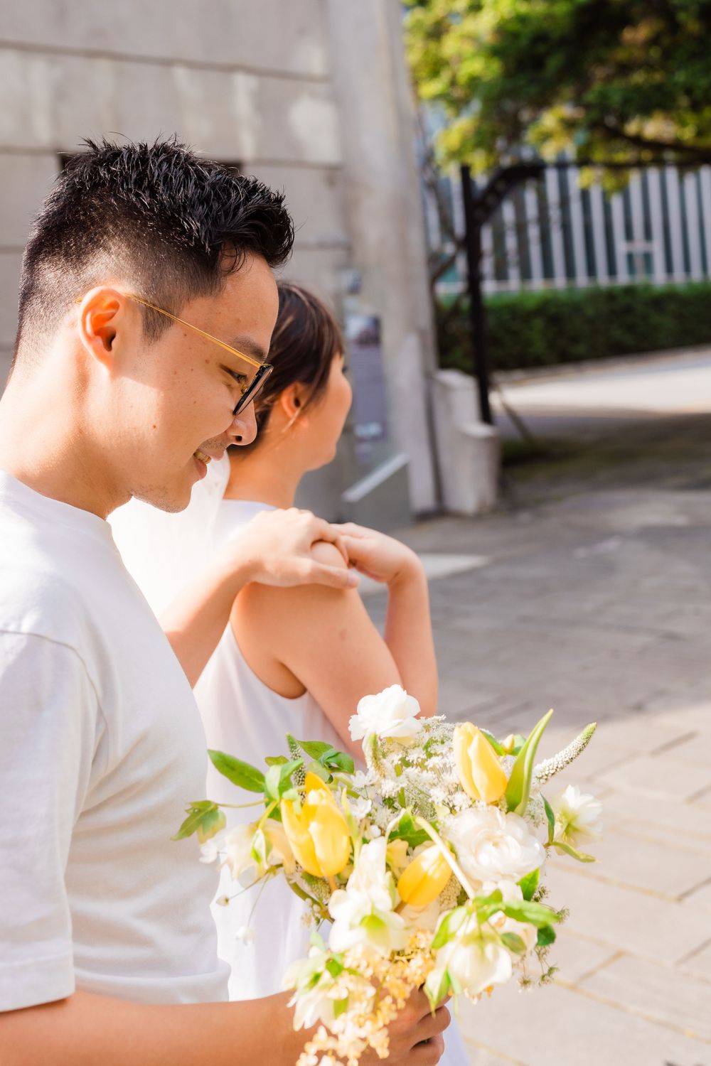 A tender moment captured between a couple with a yellow and white bouquet in an outdoor setting.