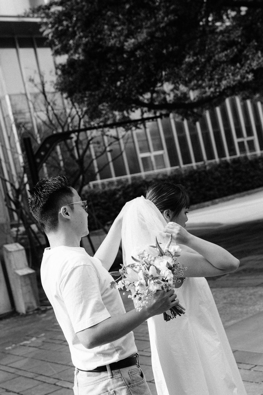 A black and white photo of a couple sharing a playful moment with a floral bouquet.
