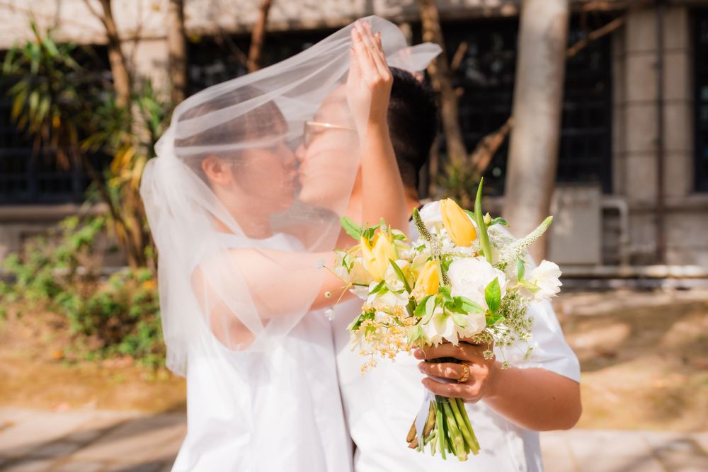 A romantic moment captured through a flowing veil with a yellow and white bouquet.
