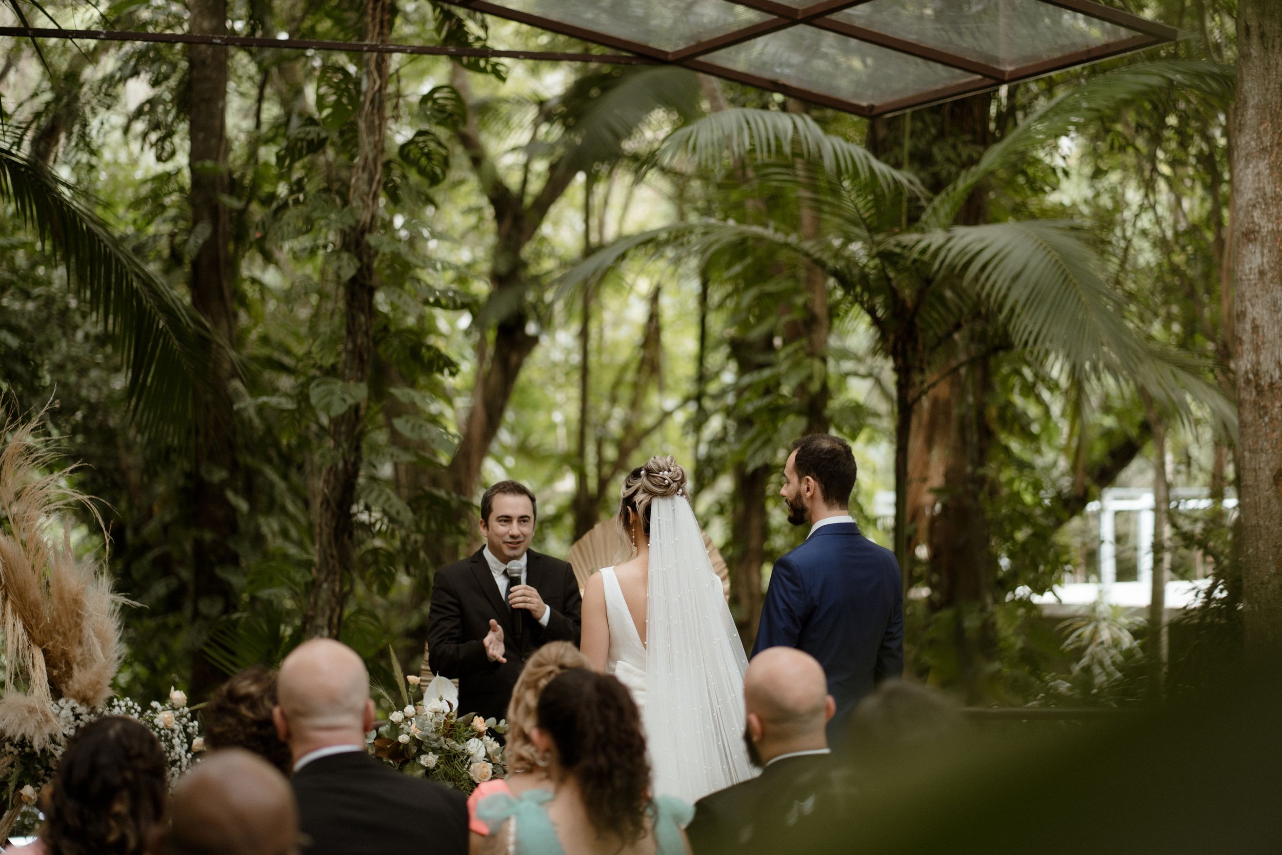 Wedding ceremony in progress under a natural forest canopy with string lights.