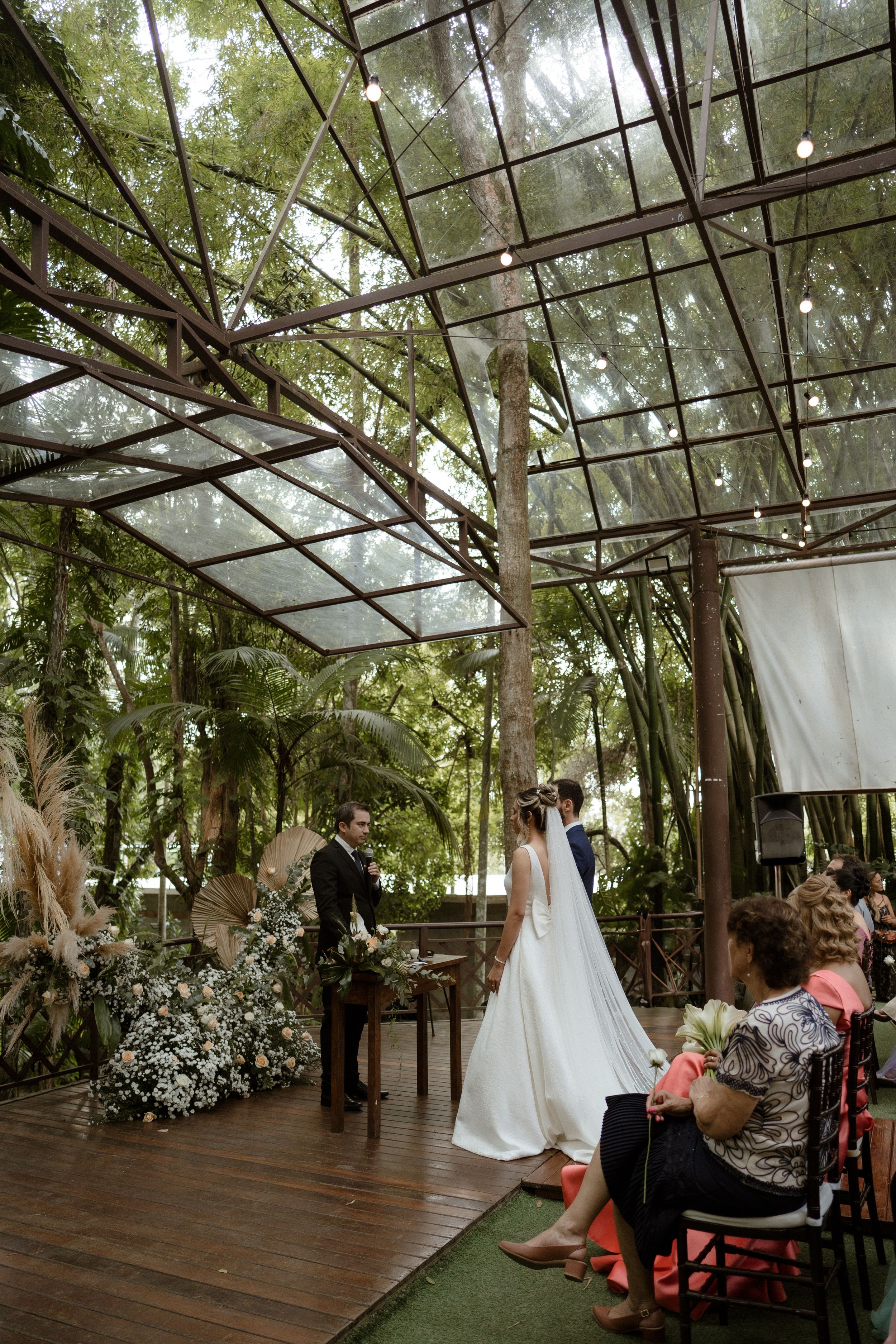 Wedding ceremony setup in a wooded venue with string lights and white fabric decor.
