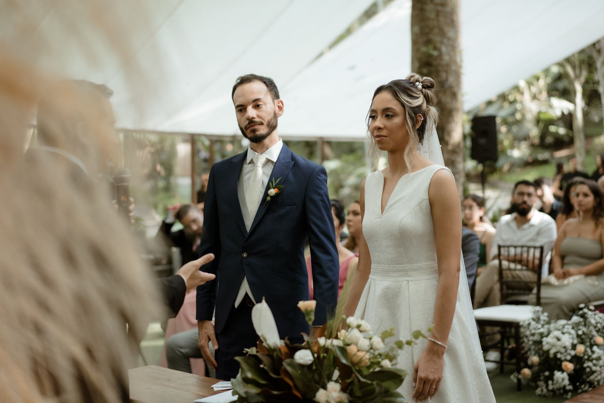 A wedding ceremony takes place in an elegant outdoor venue with floral arrangements and natural light.