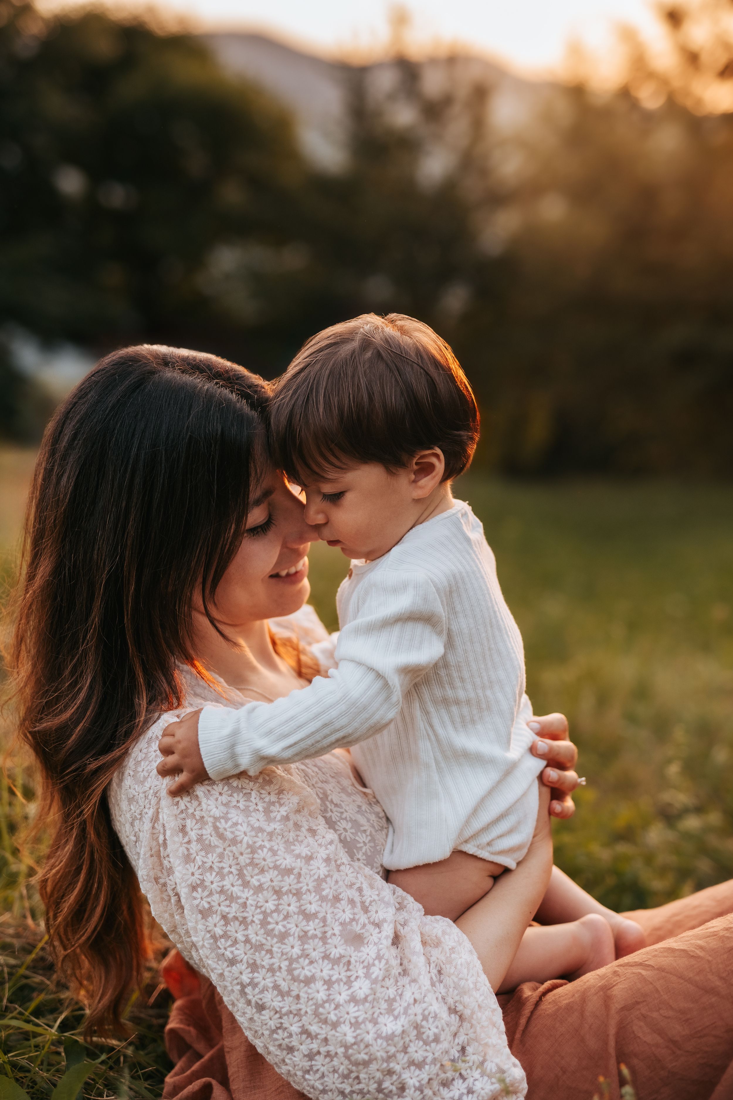 Mamma e figlio piccolo seduti in un prato al tramonto si scambiano coccole
