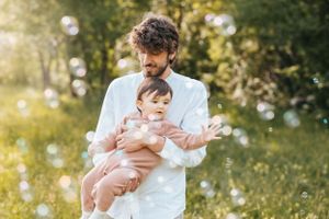 Papà e bambino in un prato verde ad aprile giocano con le bolle di sapone
