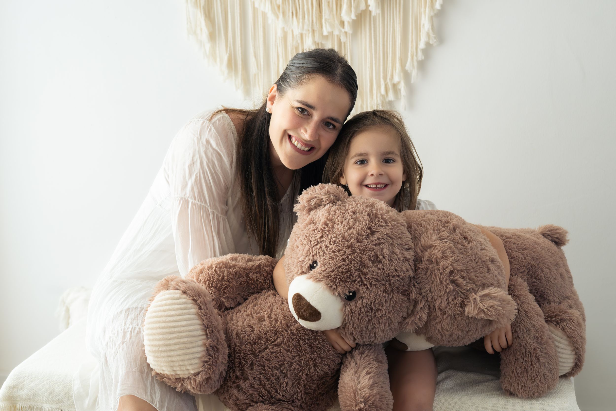 Mamma e figlia sorridono alla macchina fotografica mentre abbracciano due orsi di peluches