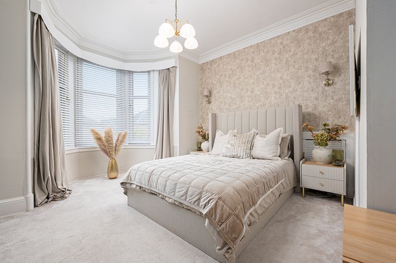 Modern white bedroom with chandelier, beige wallpaper, and soft textiles creating an elegant and cozy atmosphere.