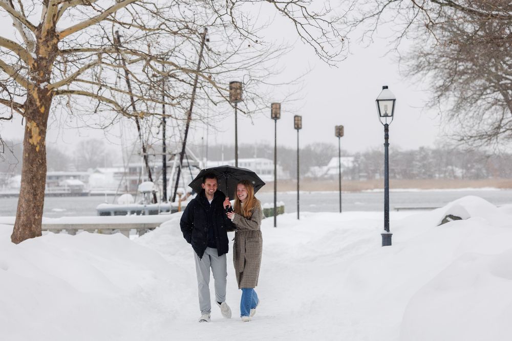People walking and playing in a snowy park landscape with lampposts along a path during winter weather.