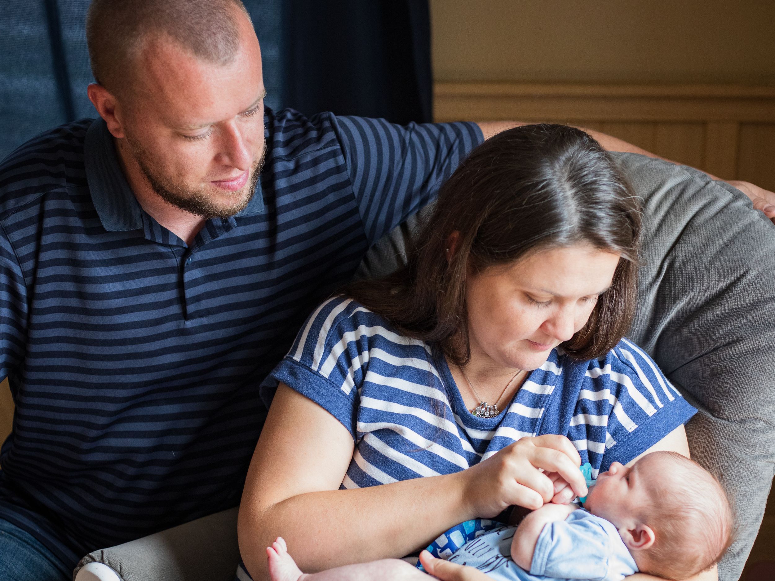A father tenderly watches as a mother holds their newborn baby in a cozy home setting.