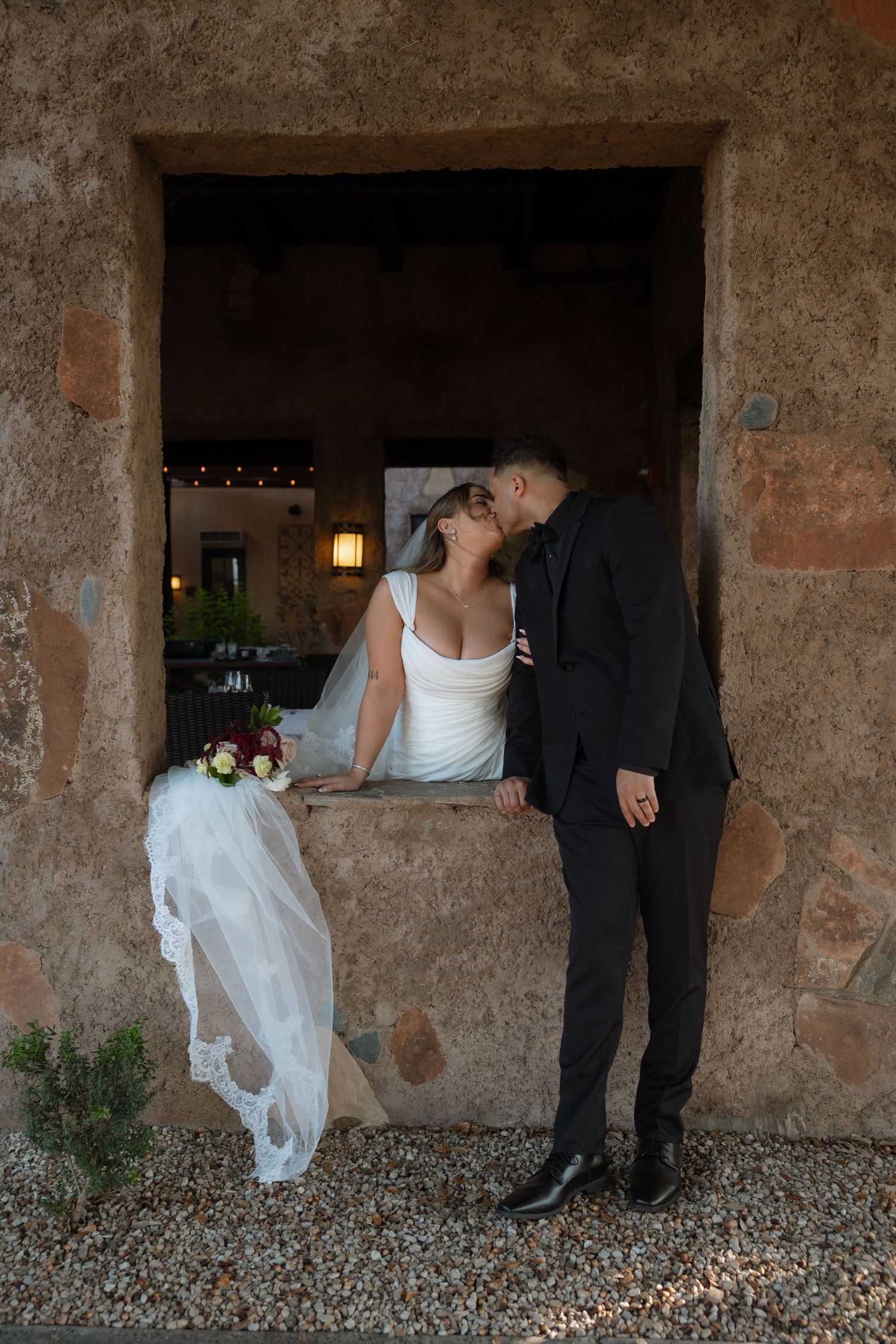 Newlywed couple walks down aisle at outdoor rooftop wedding ceremony with city buildings and sunlight in background.